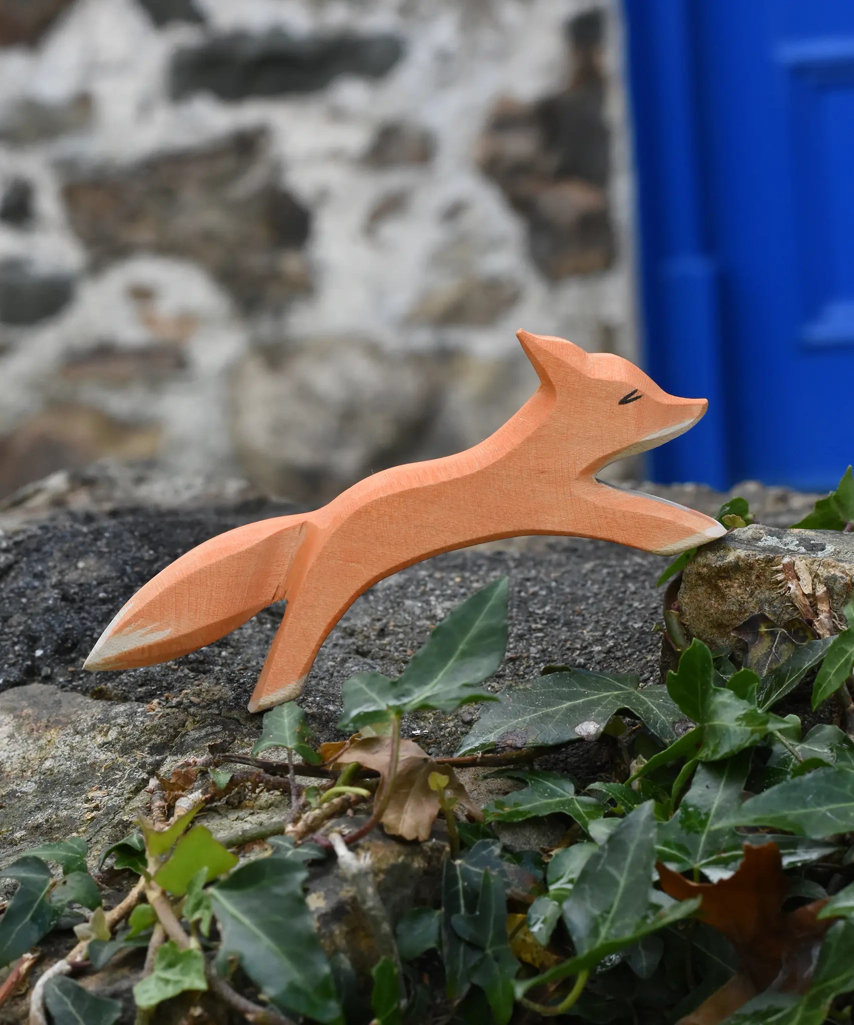 Ostheimer running fox wooden toy figure placed on a stone wall outdoors. 