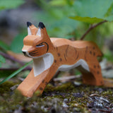 Ostheimer Wooden Running Lynx toy figure placed on a mossy surface outdoors. This expertly hand crafted wooden figure is part of a large range of wooden toys here at Babipur.