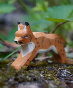 Ostheimer Wooden Running Lynx toy figure placed on a mossy surface outdoors. This expertly hand crafted wooden figure is part of a large range of wooden toys here at Babipur.