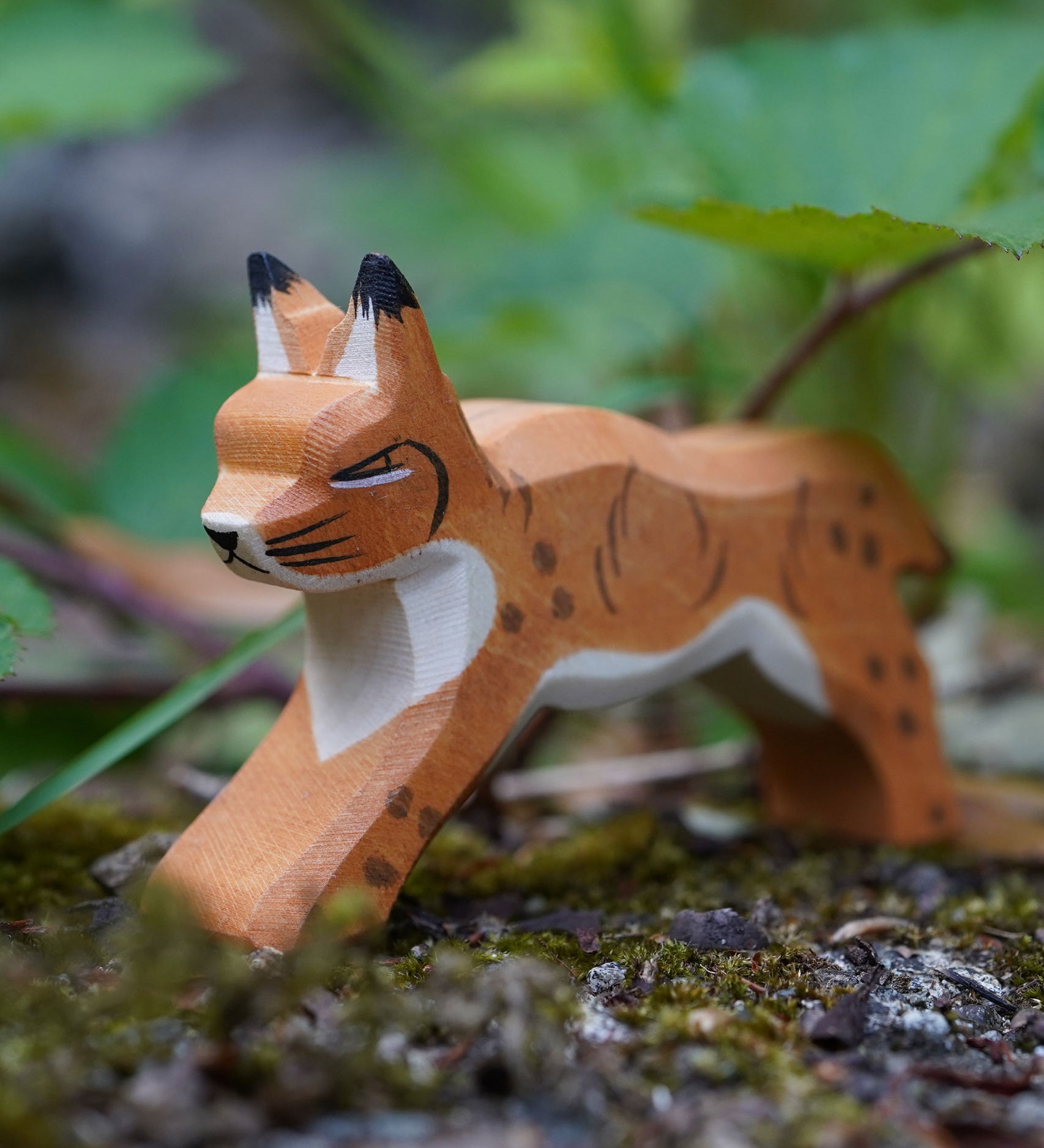 Ostheimer Wooden Running Lynx toy figure placed on a mossy surface outdoors. This expertly hand crafted wooden figure is part of a large range of wooden toys here at Babipur.