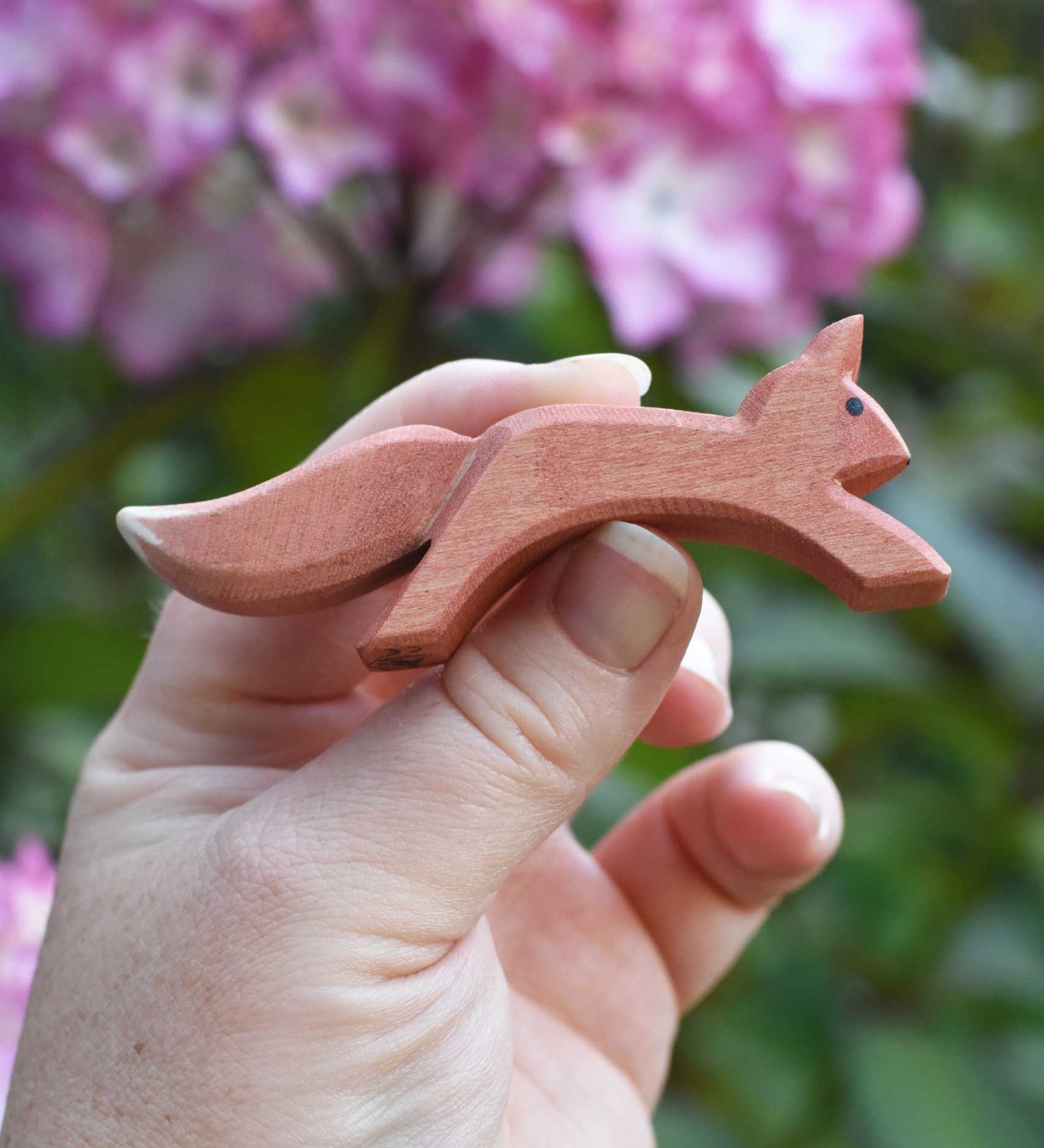 An Ostheimer running red squirrel figure shown in an adult's hand for scale. Check out our full range of expertly crafted wooden toy figures and scenery here at Babipur.