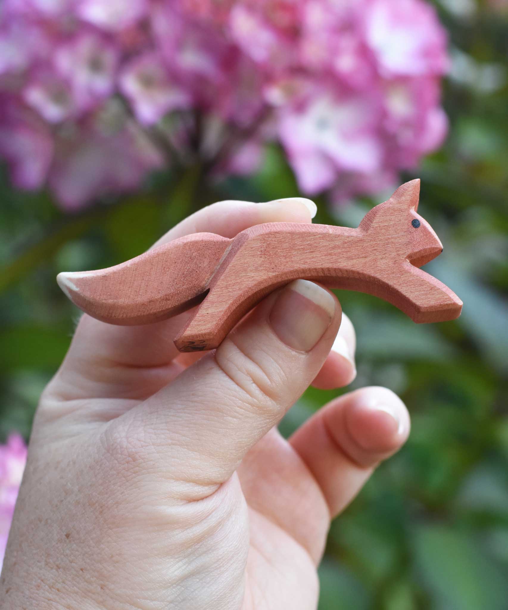 An Ostheimer running red squirrel figure shown in an adult's hand for scale. Check out our full range of expertly crafted wooden toy figures and scenery here at Babipur.