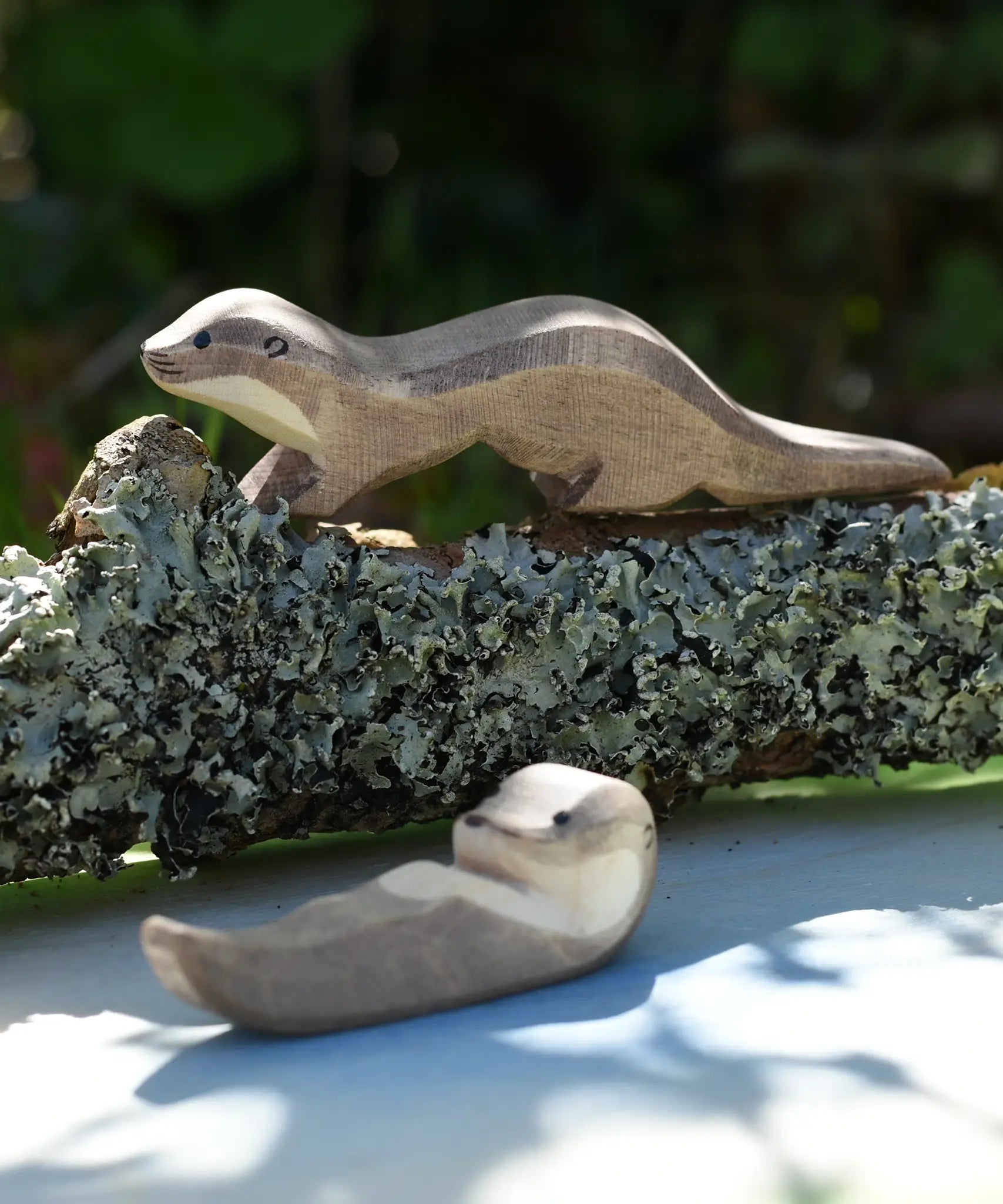 Ostheimer running sea otter wooden toy figure placed on a lichen covered branch. 