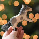 An Ostheimer shetland pony wooden toy figure in an adult's hand.  Ostheimer's range of hand crafted, heirloom quality wooden toys are available to buy at Babipur. 