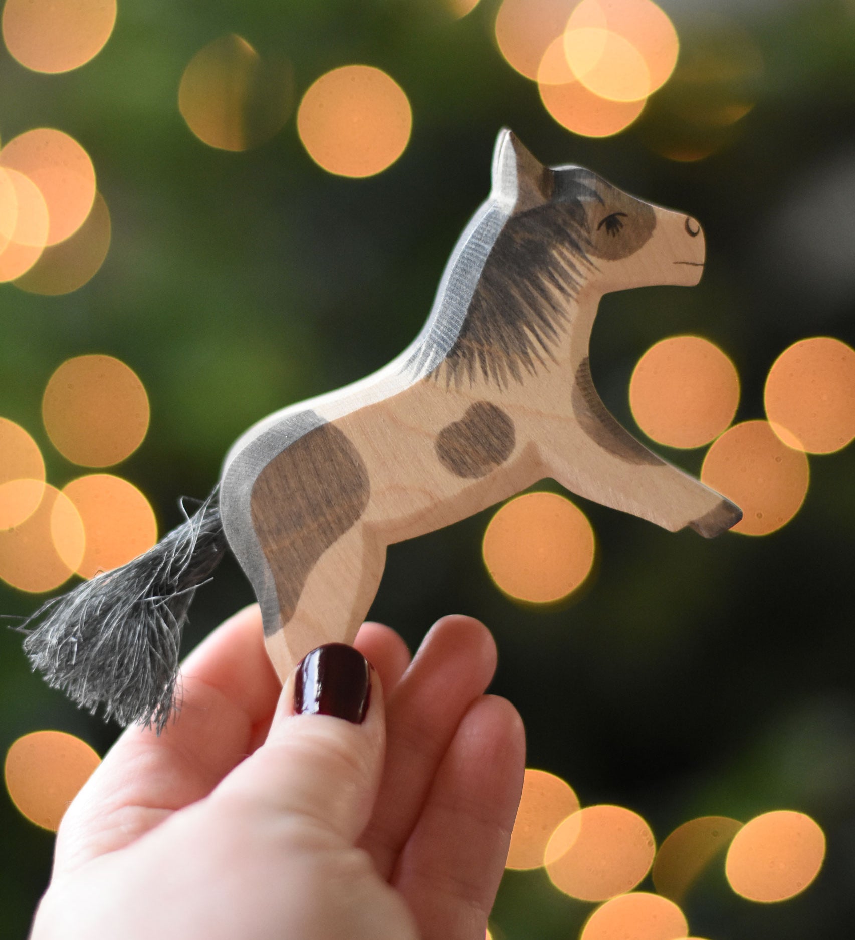 An Ostheimer shetland pony wooden toy figure in an adult's hand.  Ostheimer's range of hand crafted, heirloom quality wooden toys are available to buy at Babipur. 