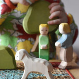 Ostheimer white running lamb wooden toy figure placed at the front of a small world play scene. Ostheimer Hansel and Gretel and scenery pieces can be seen in the background. 