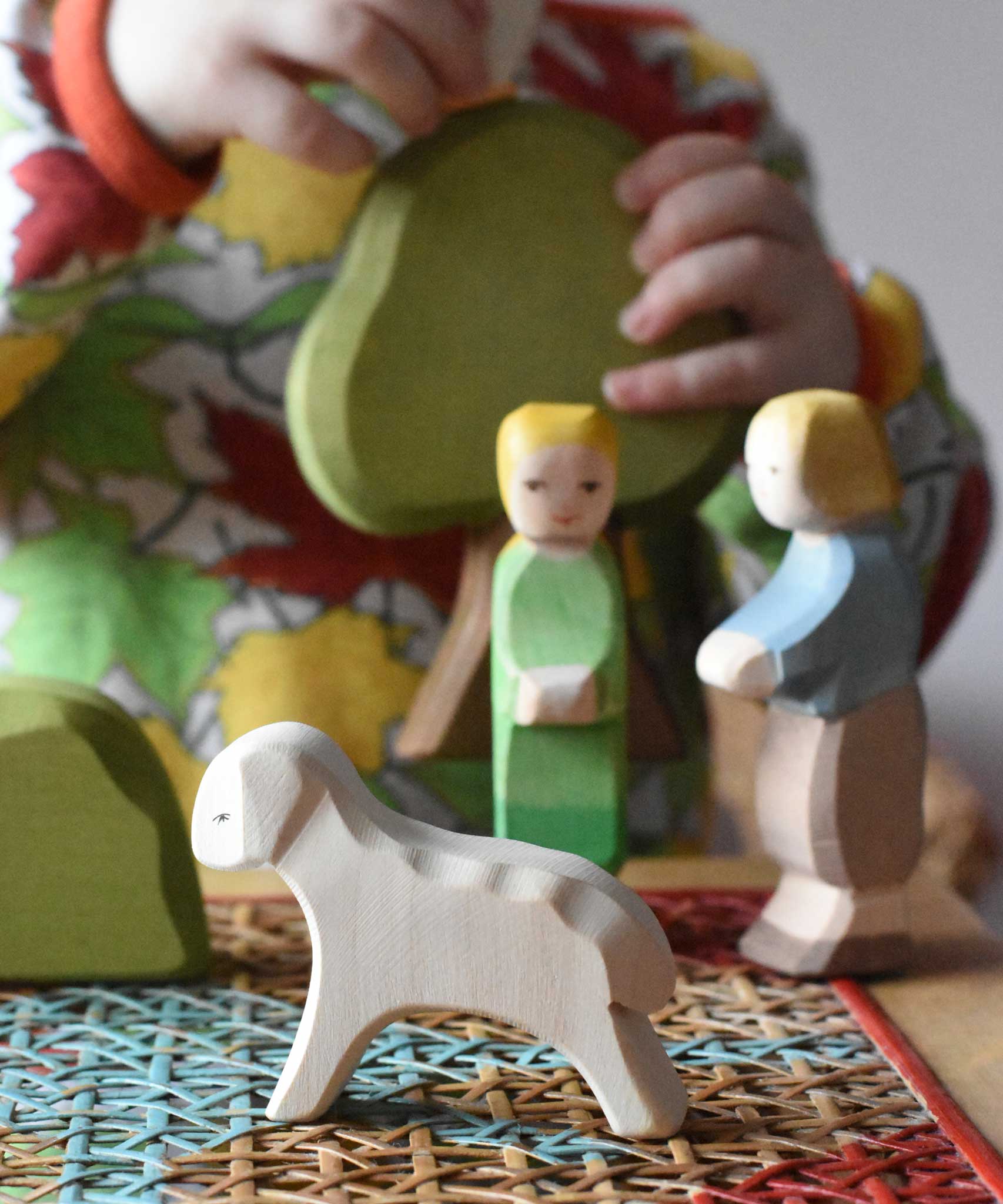 Ostheimer white running lamb wooden toy figure placed at the front of a small world play scene. Ostheimer Hansel and Gretel and scenery pieces can be seen in the background. 