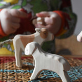 Ostheimer white running lamb wooden toy figure placed at the front of a small world play scene on a rattan top stool.