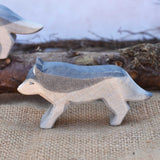 A close up of an Ostheimer running wolf wooden figure placed in a small world play scene. A full range of expertly crafted wooden toy figures and scenery are available at Babipur.