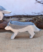 A close up of an Ostheimer running wolf wooden figure placed in a small world play scene. A full range of expertly crafted wooden toy figures and scenery are available at Babipur.