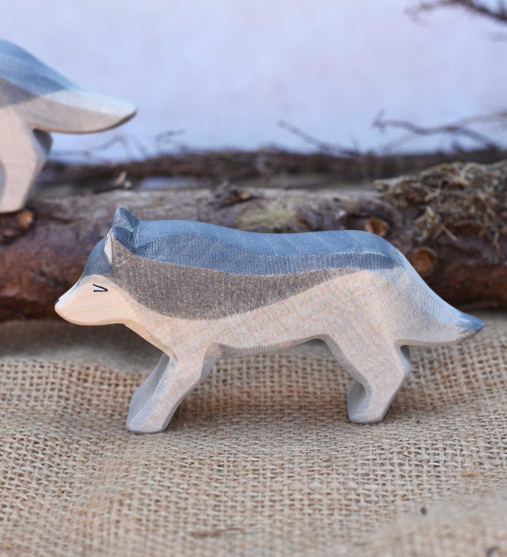 A close up of an Ostheimer running wolf wooden figure placed in a small world play scene. A full range of expertly crafted wooden toy figures and scenery are available at Babipur.