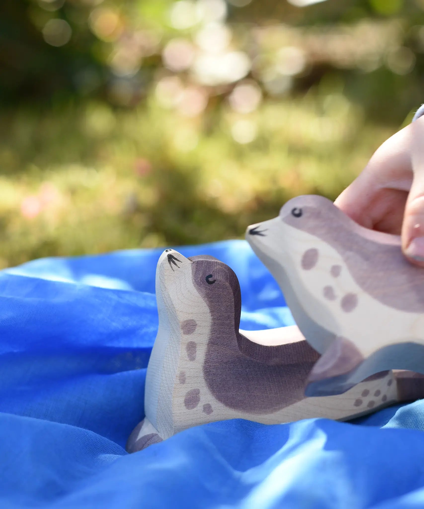 Ostheimer sea lion head high placed on a blue Laura's cotton play cloth on the Babipur garden. Child holding another sea lion in their hand.
