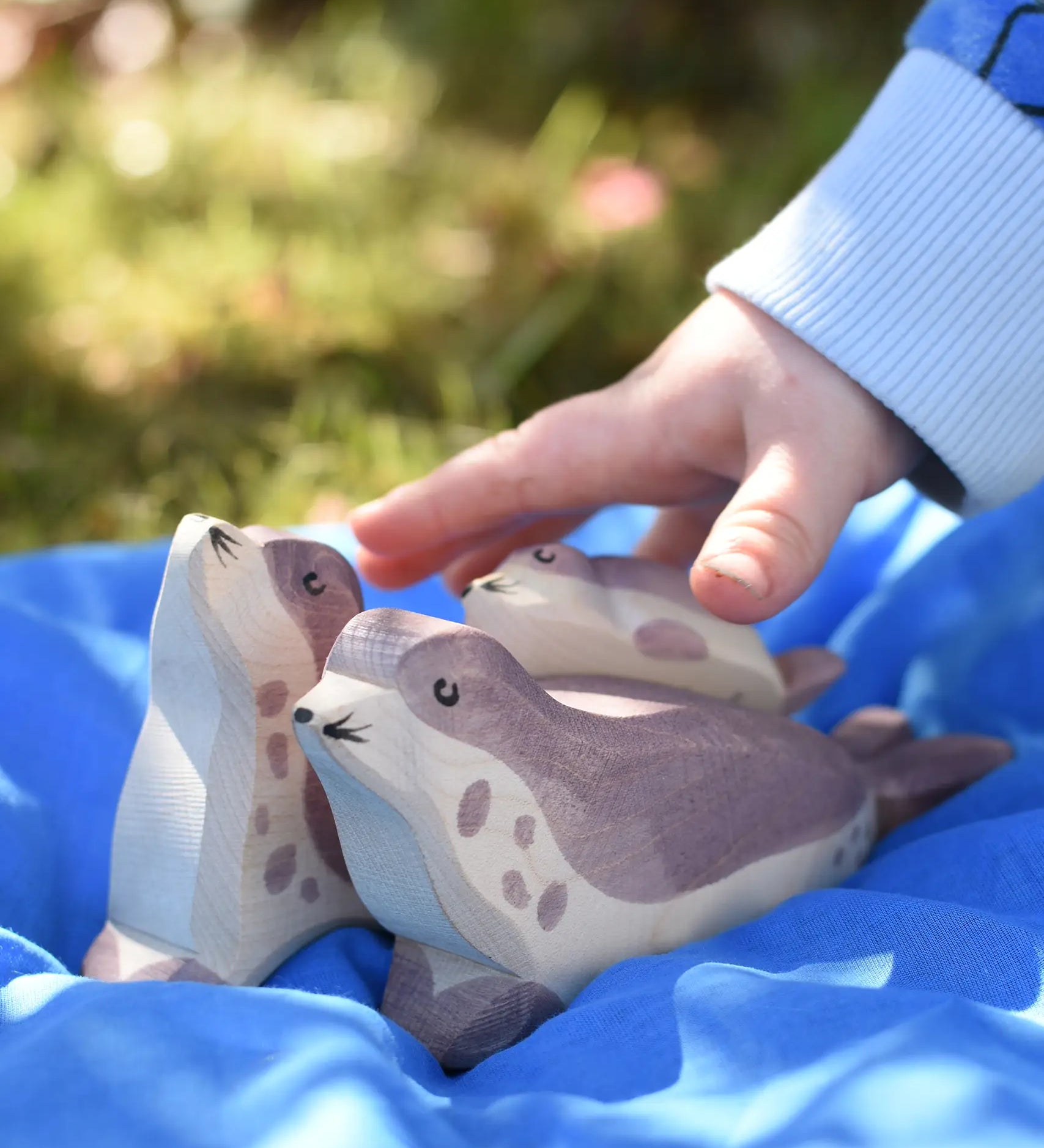 Ostheimer small sea lion pup wooden toy figure placed on the back of a bigger sea lion on a blue Laura's cotton play cloth in the Babipur garden.