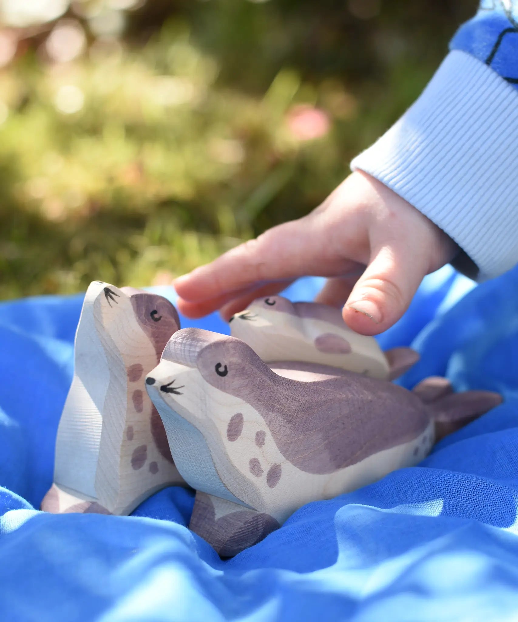 Ostheimer small sea lion pup wooden toy figure placed on the back of a bigger sea lion on a blue Laura's cotton play cloth in the Babipur garden.