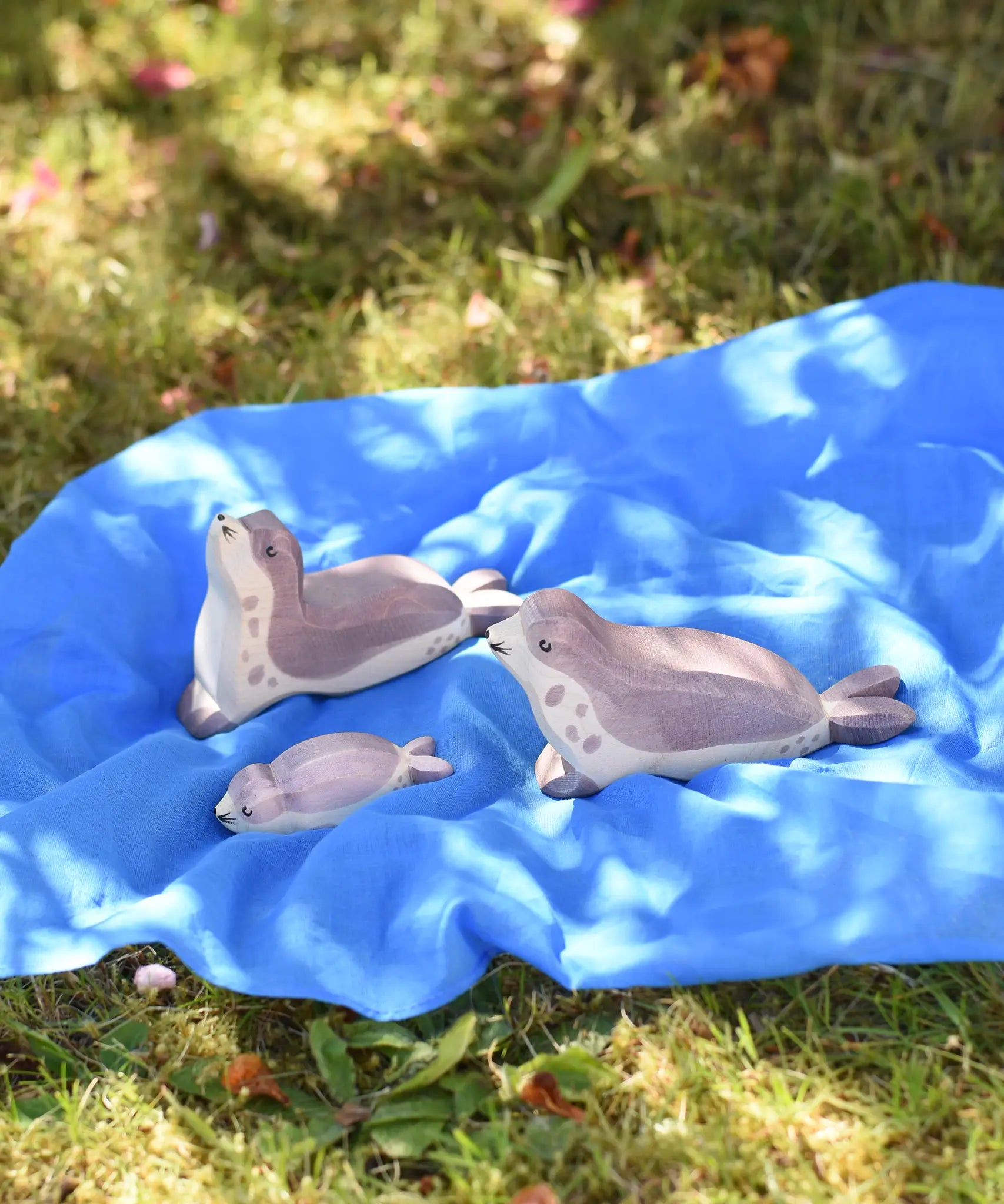 Ostheimer wooden sea lion toy figures placed on a blue Laura's cotton play cloth in the Babipur garden.