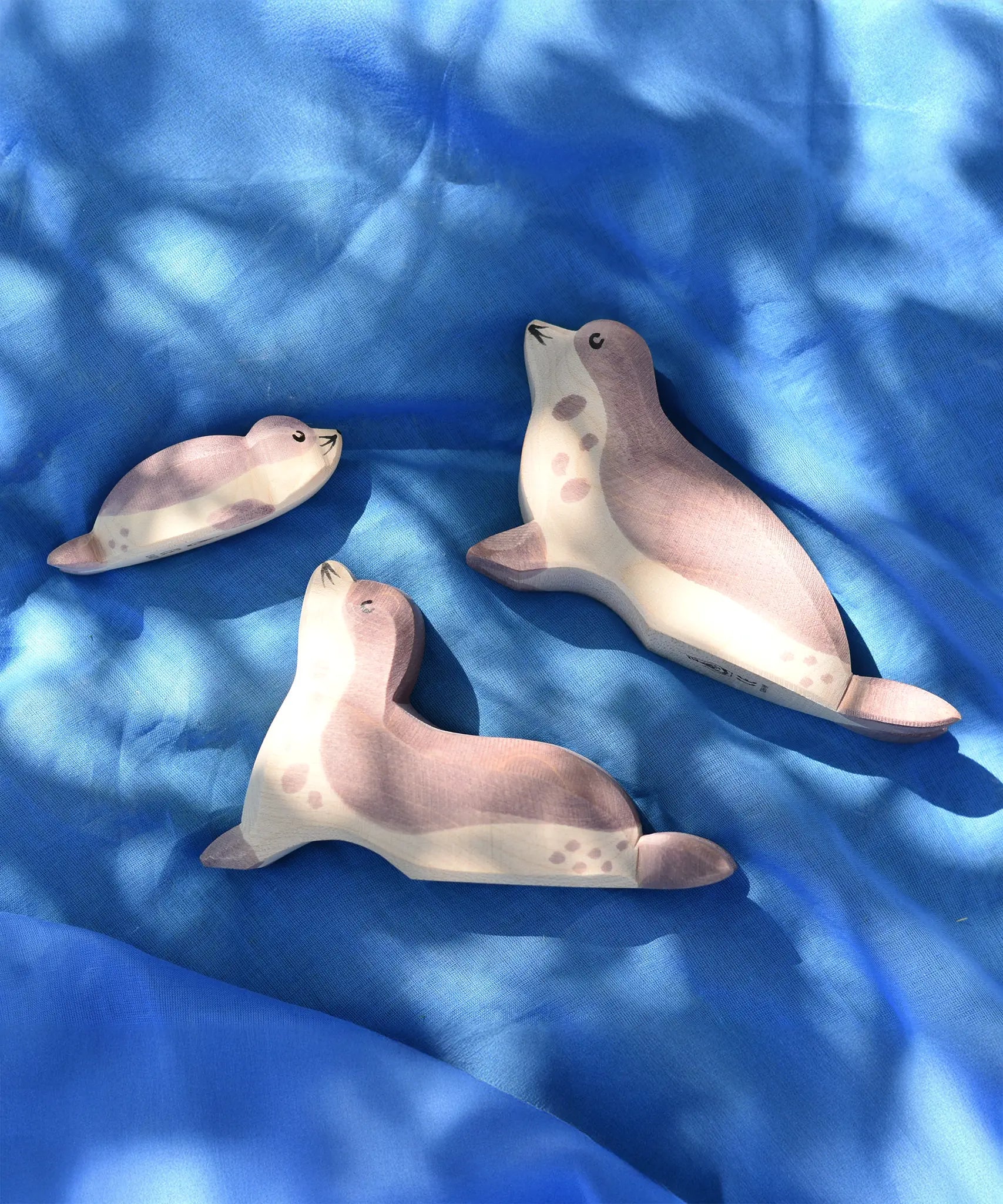 Ostheimer wooden sea lion toy figures placed on a blue Laura's cotton play cloth in the Babipur garden.