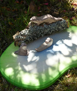 Ostheimer running sea otter wooden toy figure placed on a lichen covered branch with a small swimming and sitting otter placed in front of it. 