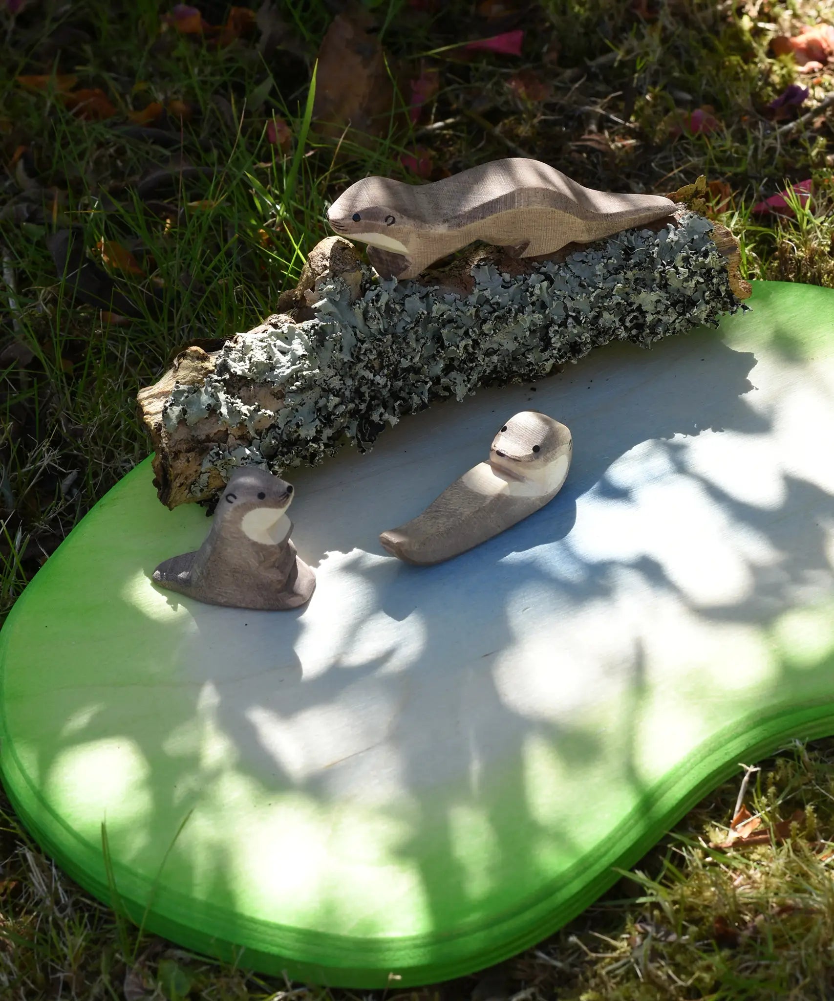 Ostheimer running sea otter wooden toy figure placed on a lichen covered branch with a small swimming and sitting otter placed in front of it. 
