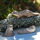 Ostheimer running sea otter wooden toy figure placed on a lichen covered branch with a small swimming and sitting otter placed in front of it. 