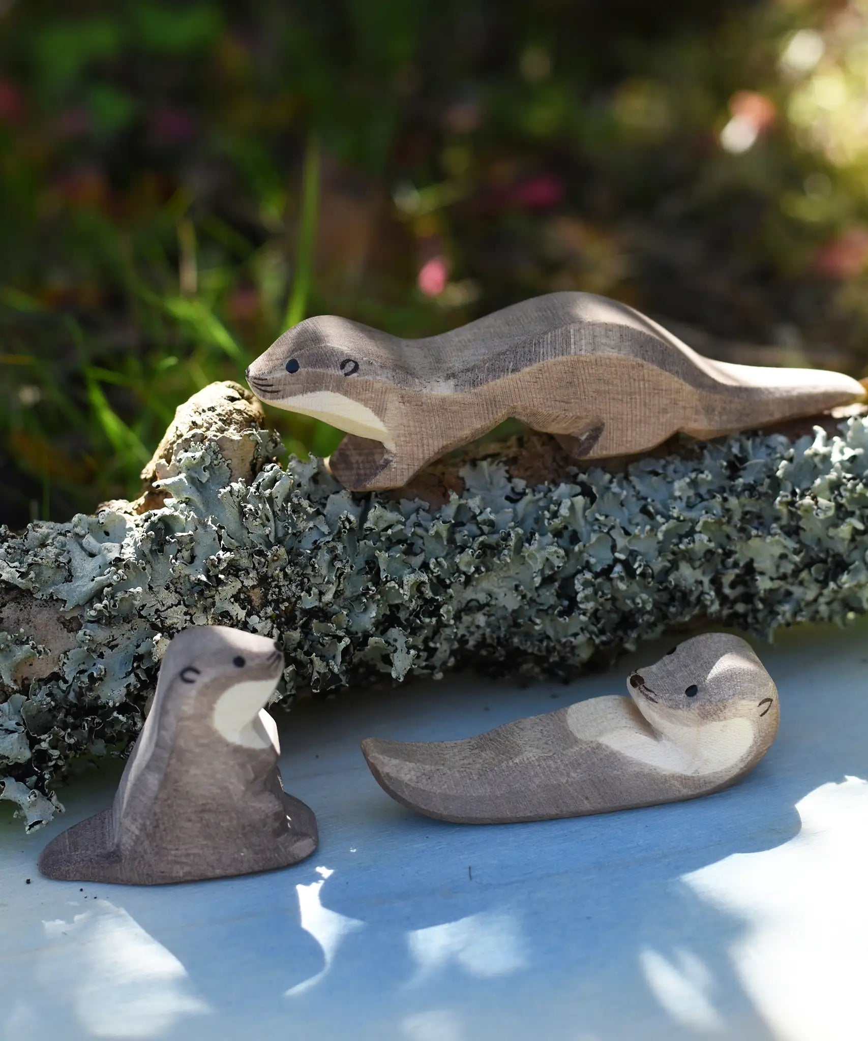 Ostheimer running sea otter wooden toy figure placed on a lichen covered branch with a small swimming and sitting otter placed in front of it. 
