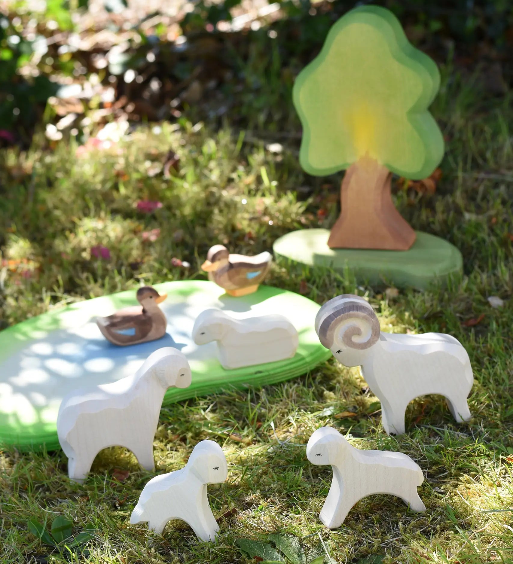 Ostheimer small world play scene with lamb, sheep, ram and duck  wooden toy figures placed on grass in the Babipur garden.