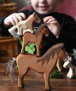 Child stacking Ostheimer horse wooden toy figures on top of each other, two brown horses and a Shetland colt on the top.