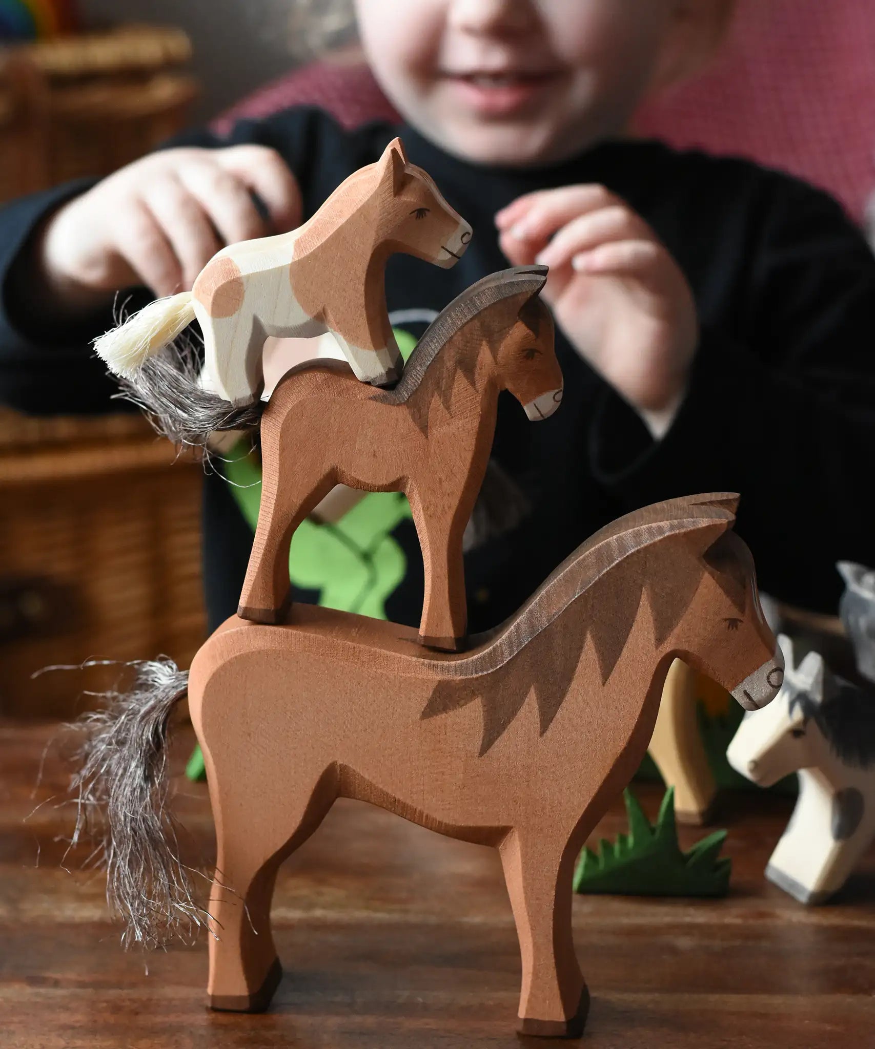 Child stacking Ostheimer horse wooden toy figures on top of each other, two brown horses and a Shetland colt on the top.