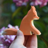 An Ostheimer sitting red fox figure shown in an adult's hand for scale. Check out our full range of expertly crafted wooden toy figures and scenery here at Babipur.