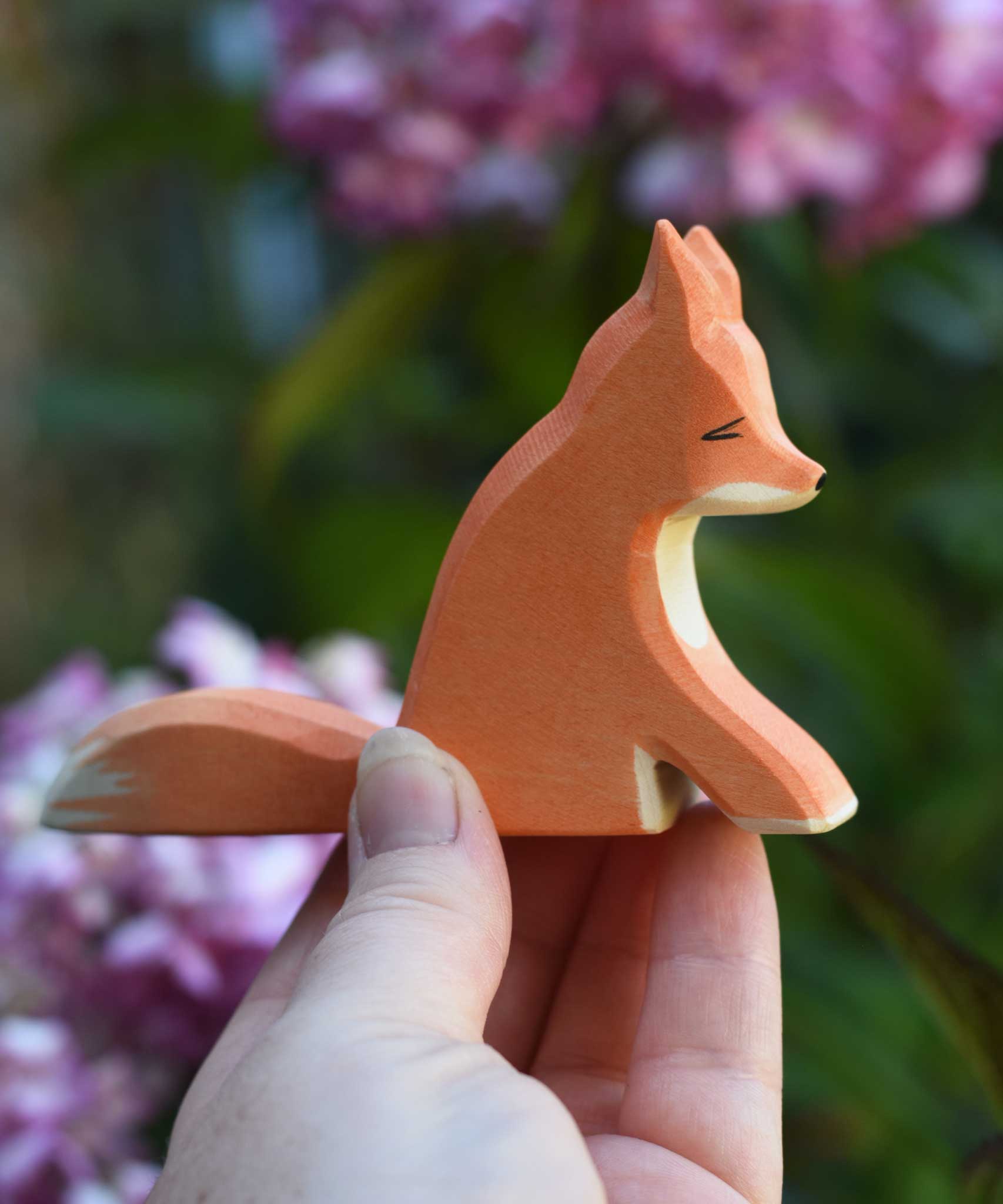 An Ostheimer sitting red fox figure shown in an adult's hand for scale. Check out our full range of expertly crafted wooden toy figures and scenery here at Babipur.