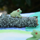 Ostheimersitting frog handmade wooden toy figure placed on a lichen covered branch piece. 