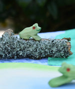 Ostheimersitting frog handmade wooden toy figure placed on a lichen covered branch piece. 