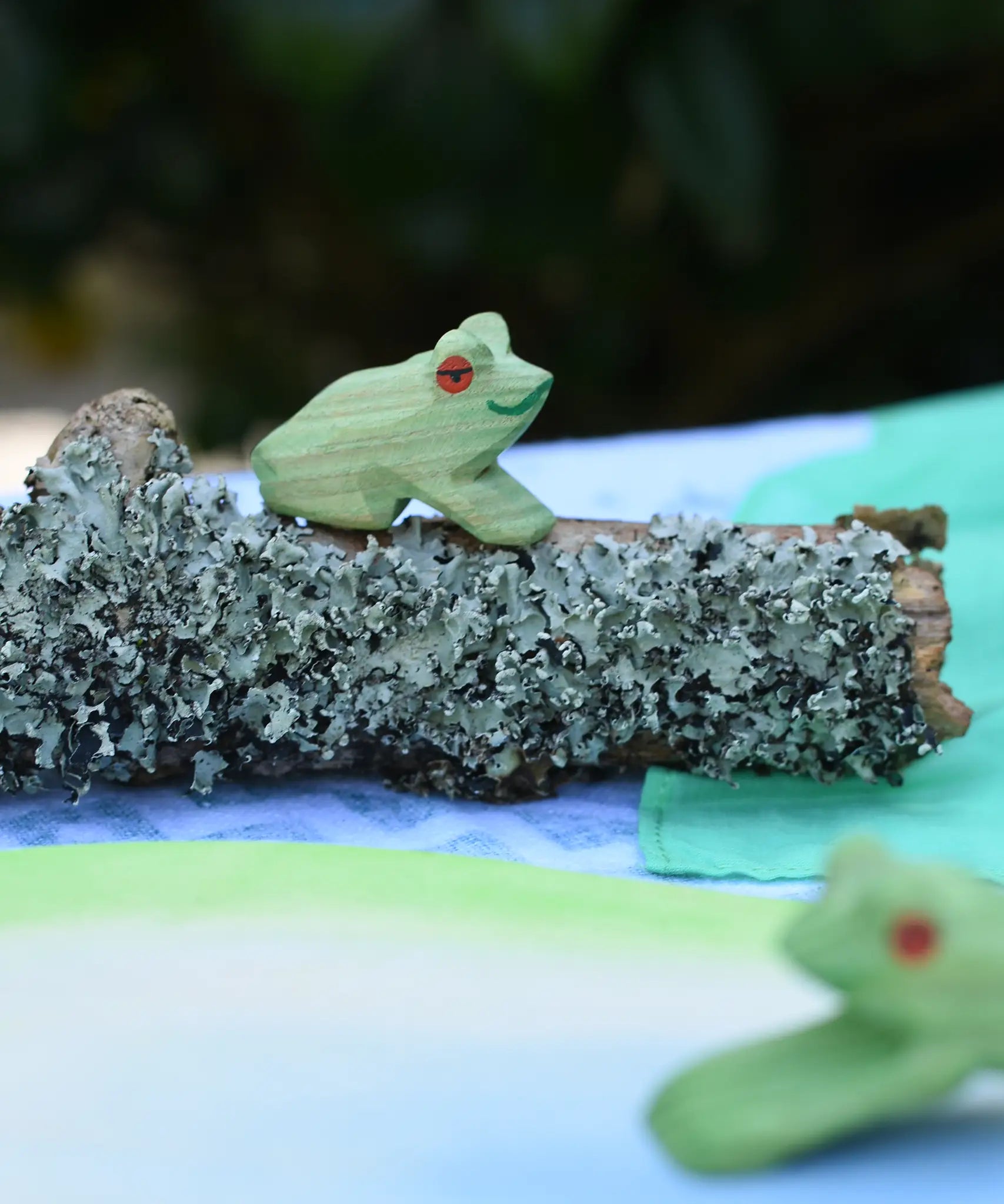 Ostheimersitting frog handmade wooden toy figure placed on a lichen covered branch piece. 