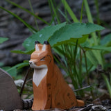 Ostheimer Wooden Sitting Lynx figure placed in front of grass and greenery outdoors. This expertly hand crafted wooden figure is part of a large range of wooden toys here at Babipur.
