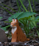 Ostheimer Wooden Sitting Lynx figure placed in front of grass and greenery outdoors. This expertly hand crafted wooden figure is part of a large range of wooden toys here at Babipur.