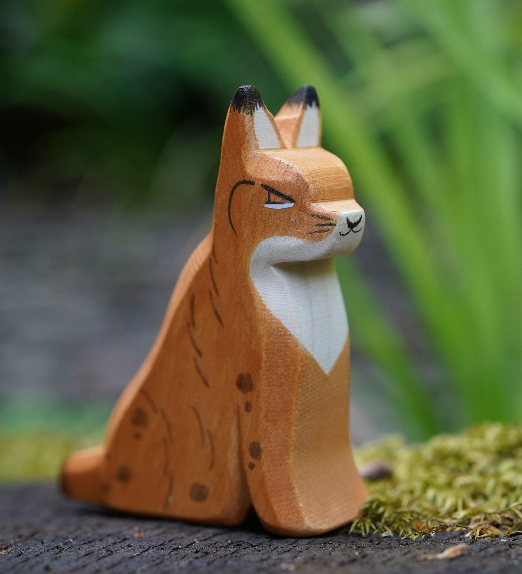 An Ostheimer sitting lynx figure placed on a mossy surface outdoors. This expertly hand crafted wooden figure is part of a large range of wooden toys here at Babipur. 