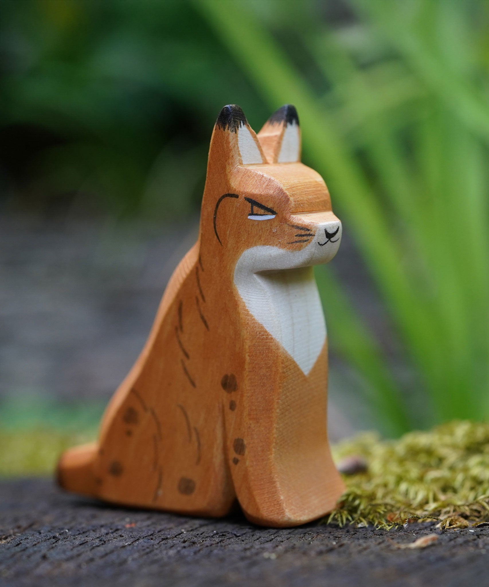 An Ostheimer sitting lynx figure placed on a mossy surface outdoors. This expertly hand crafted wooden figure is part of a large range of wooden toys here at Babipur. 
