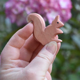 An Ostheimer Sitting Red Squirrel wooden toy figure shown in an adult's hand for scale. Check out our full range of expertly crafted wooden toy figures here at Babipur.
