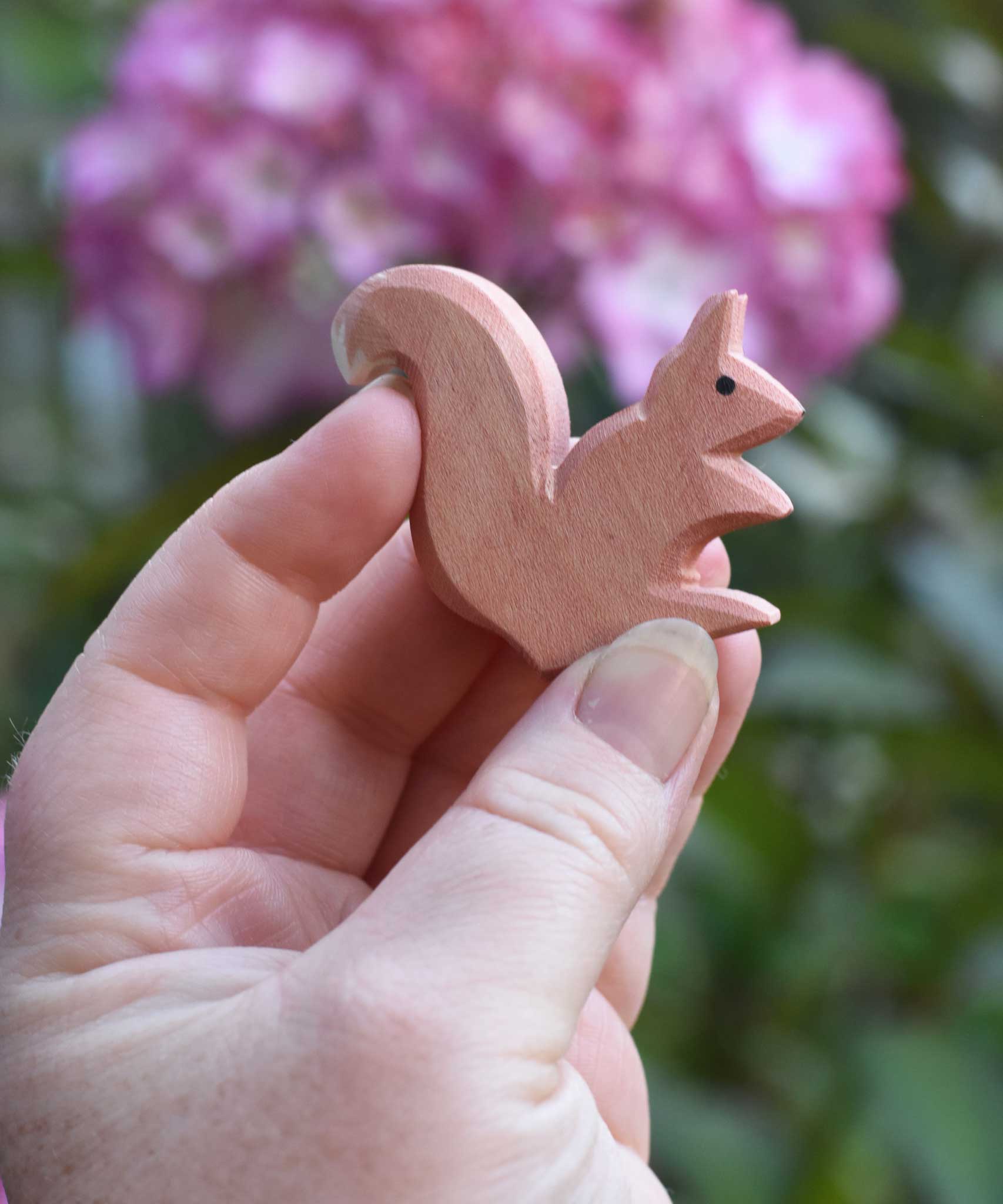 An Ostheimer Sitting Red Squirrel wooden toy figure shown in an adult's hand for scale. Check out our full range of expertly crafted wooden toy figures here at Babipur.
