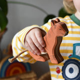Ostheimer sitting tiger wooden toy figure in a child's hand. 