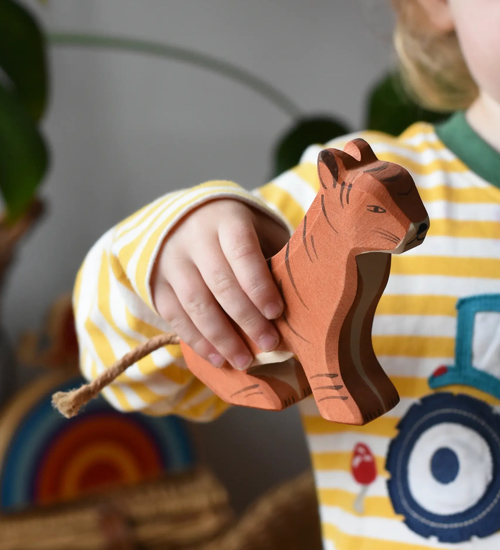 Ostheimer sitting tiger wooden toy figure in a child's hand. 