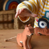 Child's hand reaching for the Ostheimer sitting tiger handmade wooden toy figure.