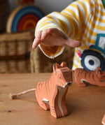 Child's hand reaching for the Ostheimer sitting tiger handmade wooden toy figure.