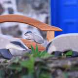 A small Ostheimer badger figures placed on a wooden toy bridge in a small world play scene. Two bigger badgers can be seen blurred in the foreground of the photo. 