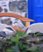 A small Ostheimer badger figures placed on a wooden toy bridge in a small world play scene. Two bigger badgers can be seen blurred in the foreground of the photo. 