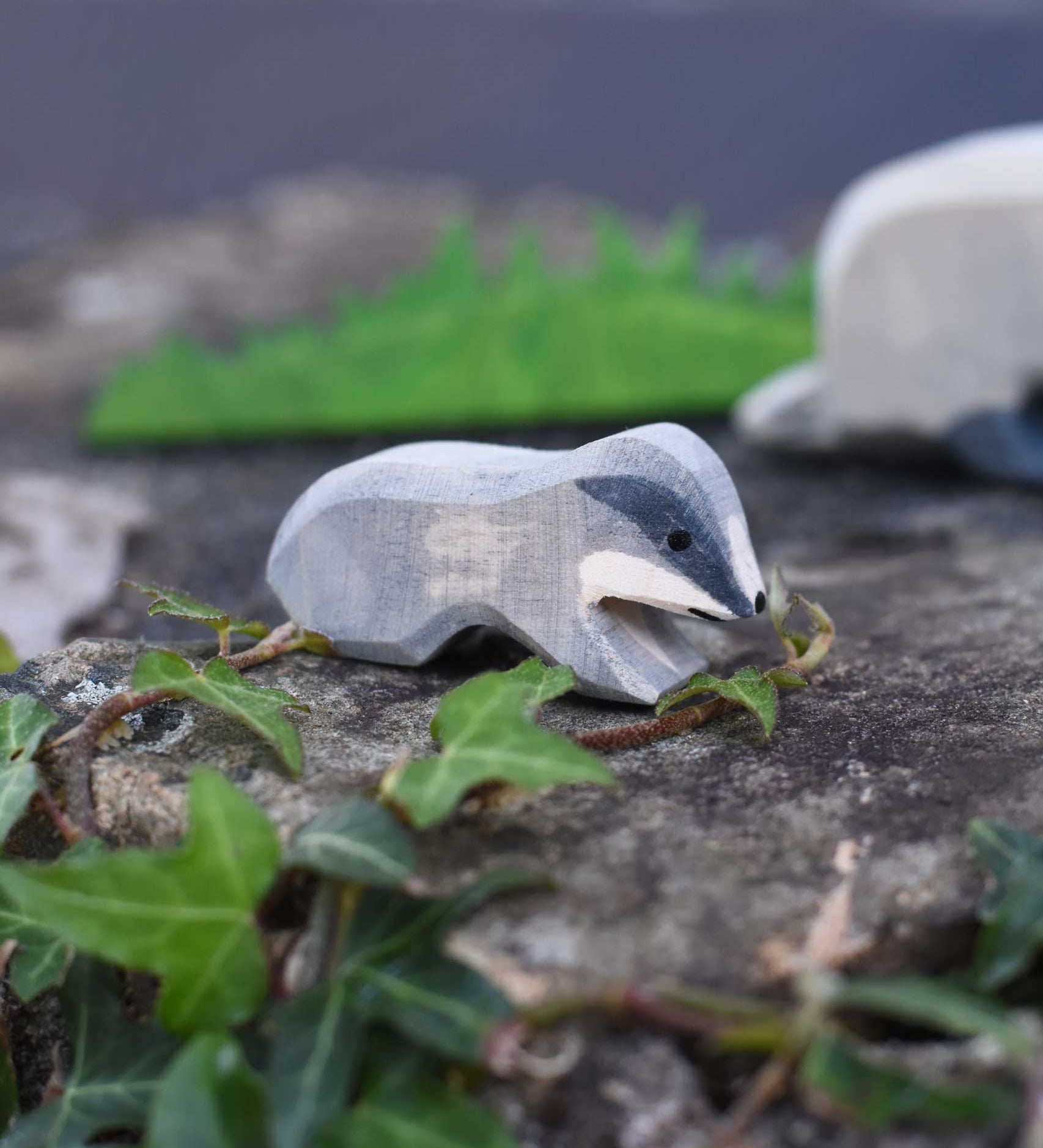 An Ostheimer small wooden badger figure placed on a stone wall outdoors. Check out our full range of wooden toy figures at Babipur.