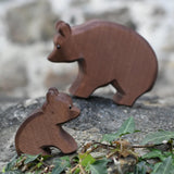 Ostheimer small sitting brown bear wooden toy figure placed on a stone wall outdoors with the large bear blurred in the background. 