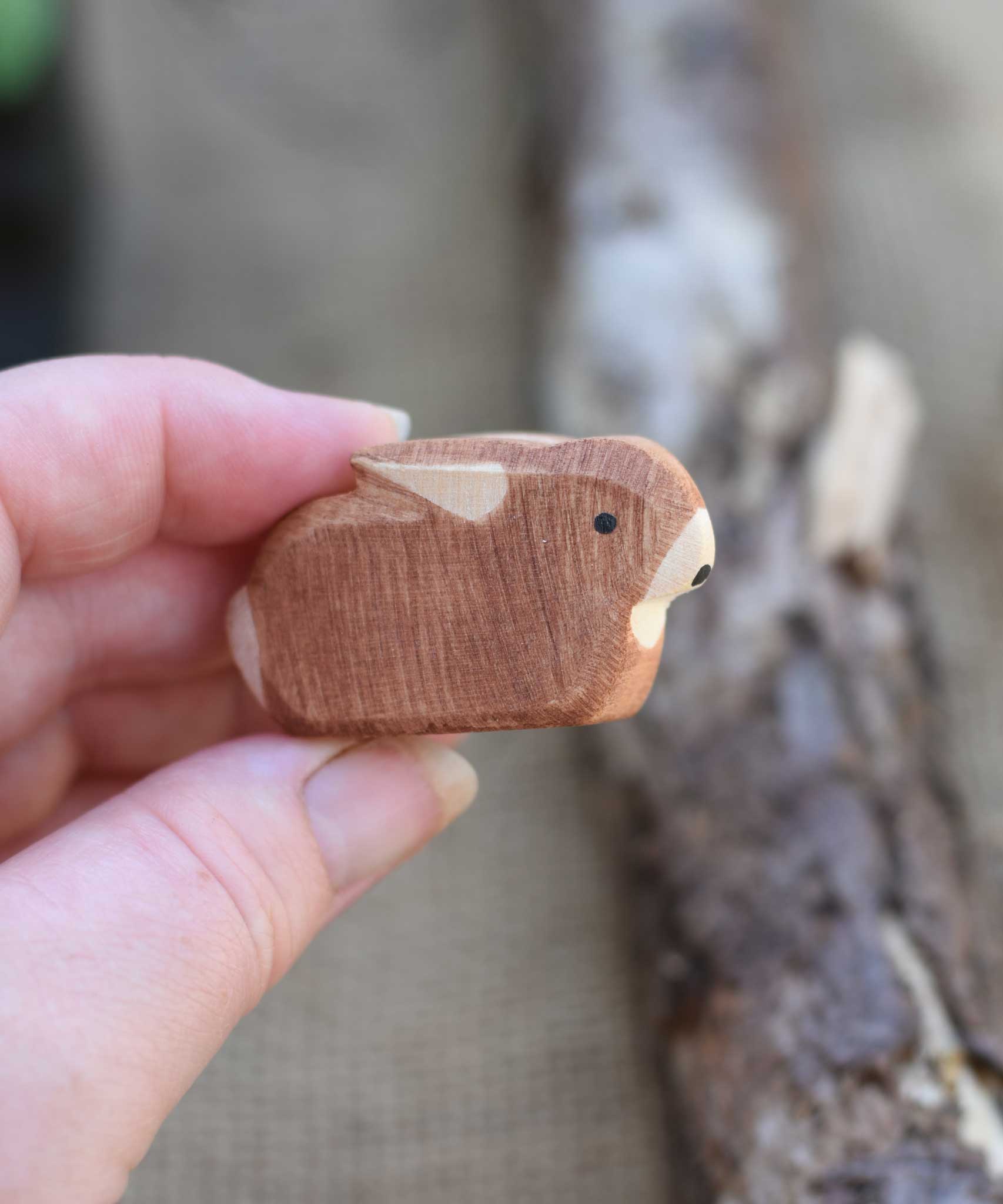 A small brown Ostheimer rabbit figure shown in an adult's hand for scale. Check out our full range of expertly crafted wooden toy figures and scenery here at Babipur.