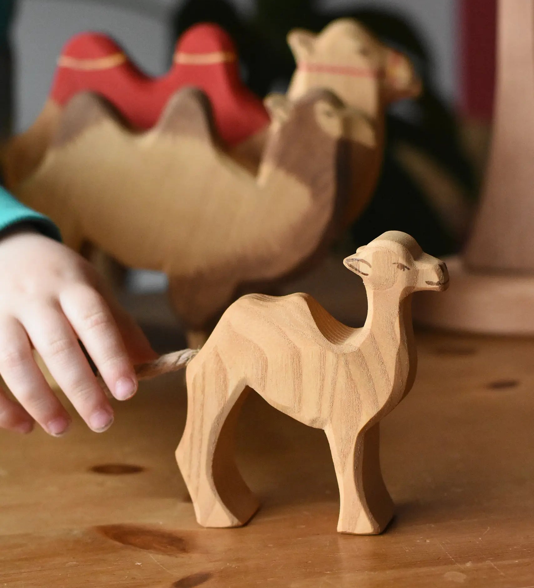 Child's hand reaching for the Ostheimer small camel wooden toy figure. 