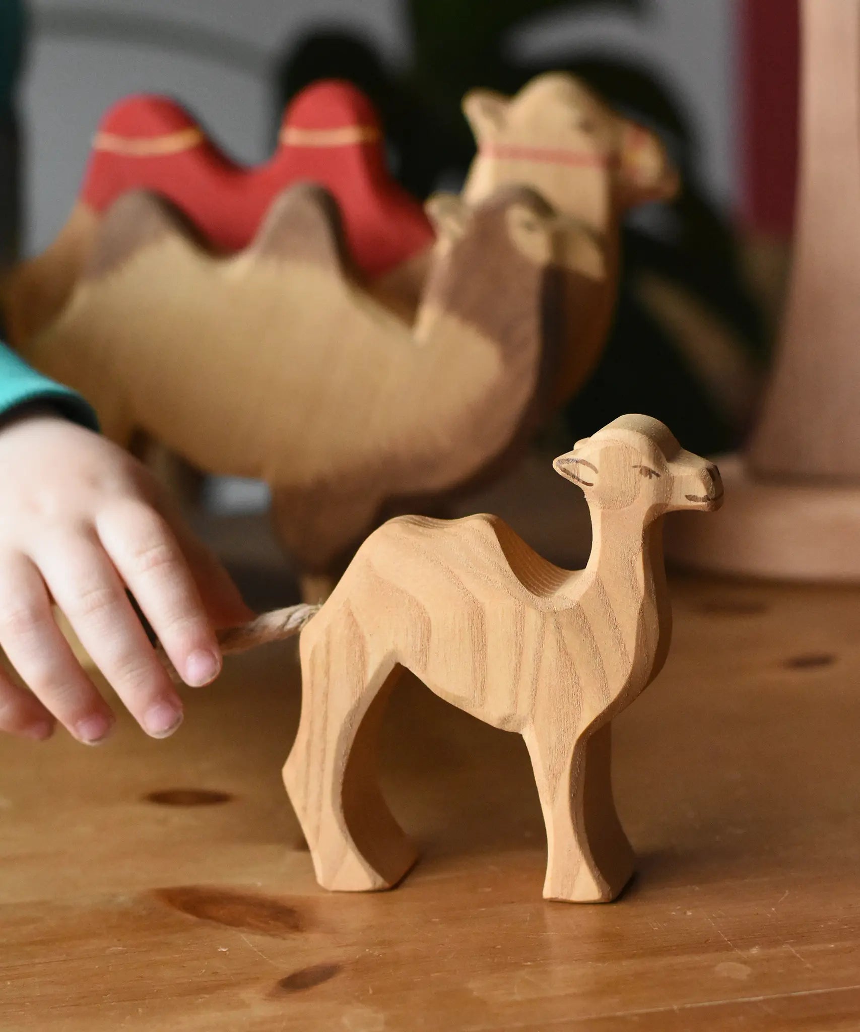 Child's hand reaching for the Ostheimer small camel wooden toy figure. 