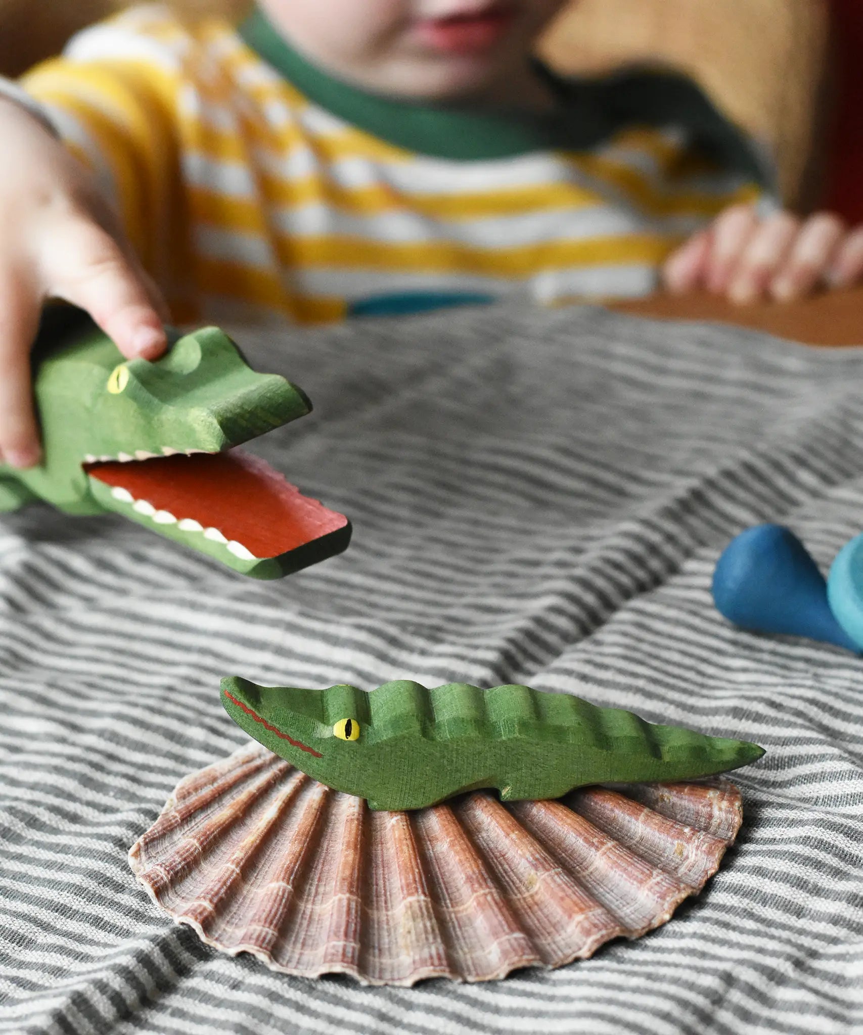 Small Ostheimer crocodile placed on a shell, a child in the background is holding the large crocodile figure. 
